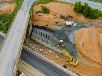 Bauingenieure und Fachkräfte auf einer Brückenbaustelle steuern ein komplexes Ingenieurbauprojekt digital mit Tablet und mobiler Software.